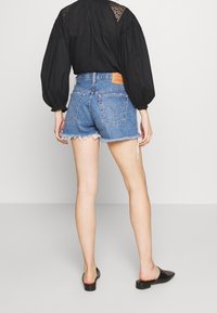 Jeansshorts med fransad fåll, ljusblå färg och två bakfickor. I kombination med en svart blus med spetsdetaljer.