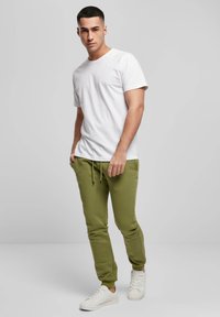 Weißes kurzärmeliges T-Shirt kombiniert mit olivgrünen Jogginghosen mit elastischem Bund und seitlichen Taschen, ergänzt durch weiße Turnschuhe.