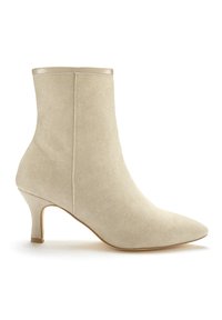 Botín de tela beige hasta el tobillo con punta afilada, tacón curvado y un acabado metálico suave en el borde superior. Superficie texturada y diseño esculpido.