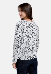 Schwarz-weiße Langarmshirt mit einem Blättermuster; aus strukturiertem Stoff; lockere Passform mit rundem Ausschnitt.