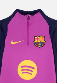 Violetinės ir tamsiai mėlynos spalvos ketvirčio užtrauktuko sportinis marškinėlis su geltonu Nike logotipu, Spotify ženklu ir FC Barcelona emblemą ant krūtinės.