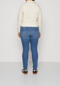 Béžová džínsová bunda s přiléhavým střihem, v kombinaci s modrými skinny džíny. Oblečení má dvě zadní kapsy a černé tenisky s hnědými podrážkami.