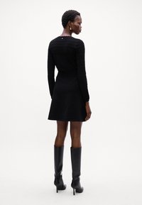 Vestito nero a maniche lunghe con maniche testurizzate, corpino aderente, gonna svasata e dettaglio con bottoni sul retro, abbinato a stivali neri con tacco al ginocchio.