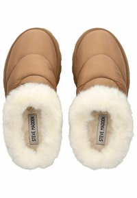 Tan slip-on slippers med quiltet design, hvid kunstpelsforing og gummisåler. Branding synlig på indre mærke.