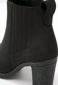 Bottines en daim noir avec des détails de couture verticale, un talon texturé noir et un logo embossé sur le côté.