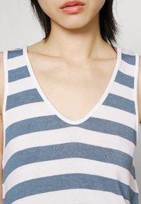 Primo piano di una persona che indossa un top senza maniche blu e bianco a righe orizzontali con scollatura a V, mostrando il collo e le labbra.