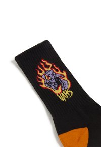 Czarna skarpeta o żebrowanej fakturze, z kolorowym wzorem płomieni i grafiką czaszki. Pomarańczowy akcent na palcu.