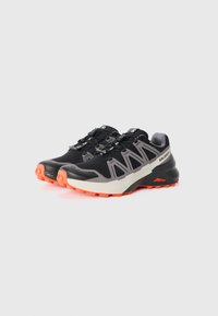 Black and gray trail running shoes with an intricate mesh design, featuring orange accents and a rugged sole for traction.