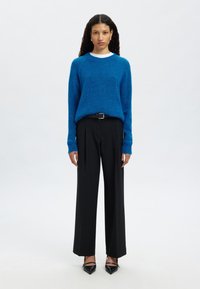 Modri puhasti pulover, črne široke hlače z gubami in črni čevlji s špičastim podplatom. Obleka vključuje belo notranjo ovratnico.