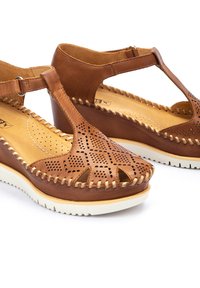 Sandali con zeppa in pelle marrone, caratterizzati da un design perforato e dettagli cuciti. Presentano una fascia a T e una suola in gomma bianca per il massimo comfort.
