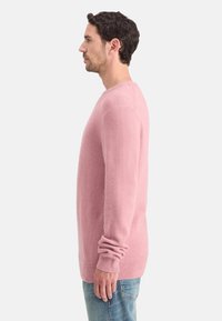 Suéter rosa claro de manga larga, con puños y dobladillo acanalados, confeccionado en un material suave y texturizado, presenta un escote redondo y un ajuste relajado.