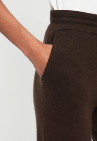 Brązowe spodnie z dzianiny o miękkiej fakturze, z wysokim stanem i bocznymi kieszeniami. Materiał wydaje się ciepły i wygodny.