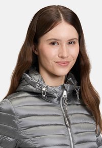 Zilveren pufferjack met een capuchon, voorzien van horizontale quiltstiksels, een ritssluiting en metalen accenten op de rits en verstelbare delen.