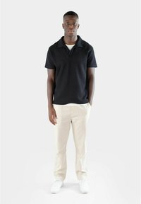 Svart texturerad polo-tröja med krage, i kombination med ljusbeige byxor och vita sneakers. Enkel, modern design utan mönster.
