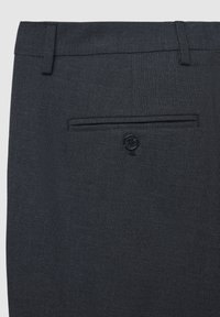 Pantaloni scuri su misura con tessuto strutturato, caratterizzati da una tasca posteriore con bottone e una cintura liscia. Il colore è un blu navy profondo.