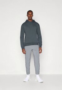 Tmavě šedá mikina s kapucí, s přední kapsou a žebrovanými manžetami, doplněná světle šedými zúženými kalhotami. Outfit doplňují bílé tenisky.