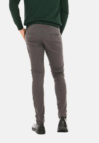 Pantaloni slim-fit grigi con tasche posteriori e una texture liscia, indossati con scarpe nere, visti da dietro.