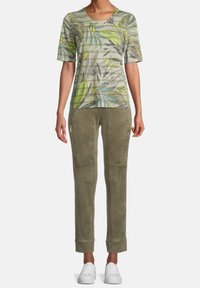 Kortärmad grön och grå blommig t-shirt i kombination med olivgröna slim-fit byxor med dragkedjor och mudd, bärs med vita sneakers.