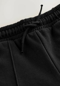 Schwarze Baumwoll-Jogginghosen mit elastischem Bund, verstellbarem Zugband und zwei seitlichen Taschen. Glatte Textur und einfaches Design.