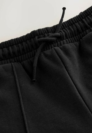 Schwarze Baumwoll-Jogginghosen mit elastischem Bund, verstellbarem Zugband und zwei seitlichen Taschen. Glatte Textur und einfaches Design.