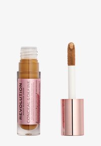Correcteur liquide dans un tube transparent avec une étiquette rose. Présente un applicateur blanc et duveteux. La couleur est beige chaud avec une finition mate.