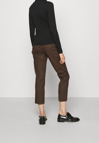 Svart långärmad topp kombinerad med bruna korta byxor och svarta skor. Mjukt tyg, figurnära design och subtila detaljer på skorna.