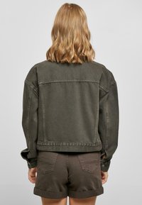 Olive green denim jacket with a loose fit, long sleeves, and visible stitching details. Paired with matching brown shorts.