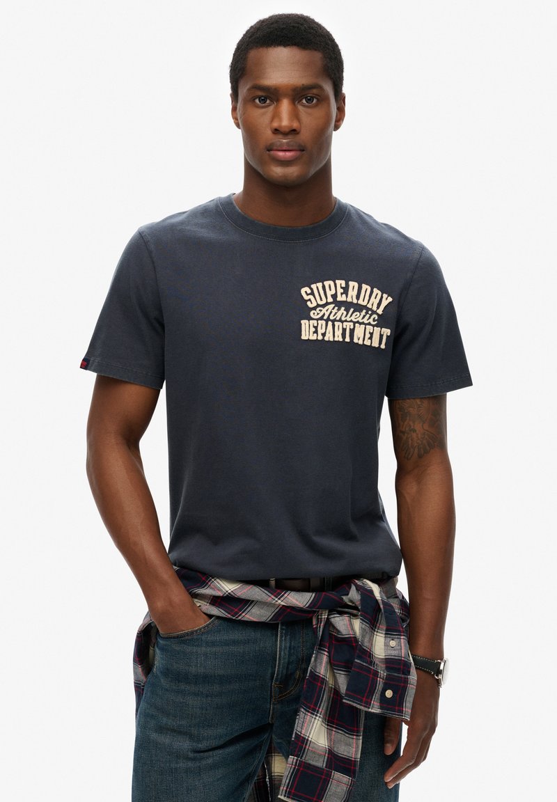 Marin bomull t-shirt med rund halsringning och ett ljusfärgat grafiskt tryck med texten "Superdry Athletic Department" på bröstet.