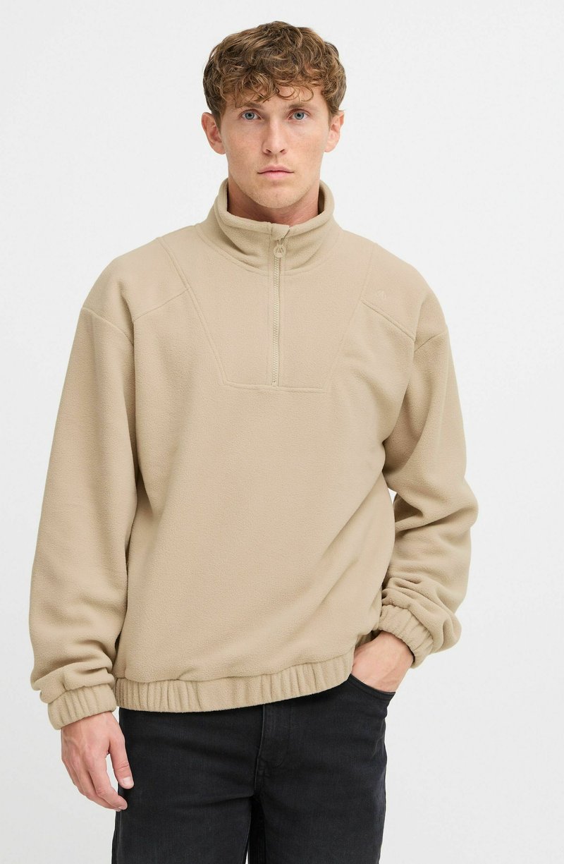 Beige fleece pullover med halvdækkende lynlås krave, elastisk søm og manchetter; har et mønstret forpanel og en afslappet pasform.