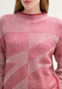 Gestrickter Pullover in verschiedenen Rosa- und Weißtönen, mit vertikalen und diagonalen Streifenmustern. Leichter Stoff mit gerippter Textur.