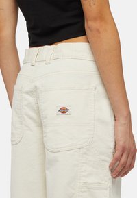 Krämfärgade kordbyxor med hög midja, med framträdande fickor och en "Dickies" logotyppatch på bakfickan.