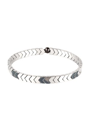 Silberfarbener Armreif mit ineinandergreifenden Chevron-förmigen Gliedern und einem kleinen runden schwarzen Magnetverschluss, isoliert auf weißem Hintergrund.