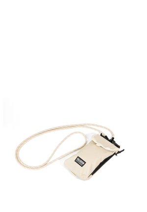 Petite pochette beige à bandoulière avec fermeture éclair noire et sangle en corde réglable, portant la marque Palladium sur le devant.