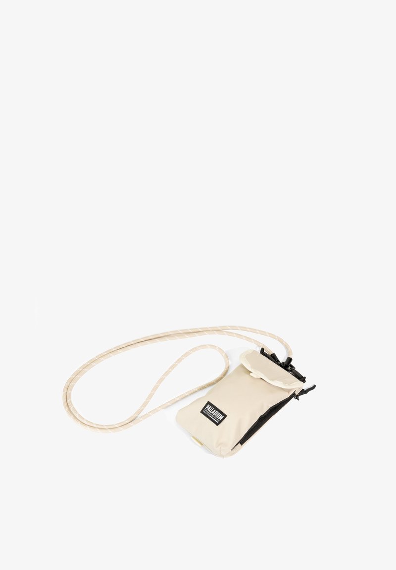 Petite pochette beige à bandoulière avec fermeture éclair noire et sangle en corde réglable, portant la marque Palladium sur le devant.