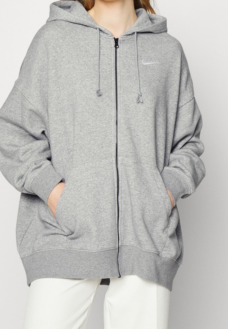 Haut à capuche zippé gris en tissu doux, doté d'une capuche, de poches kangourou et d'un logo Nike minimaliste sur la poitrine.