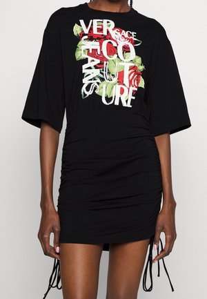 Robe noire drapée avec manches larges, graphique de rose rouge et texte blanc superposé lisant "VERSACE COUTURE" sur le devant.