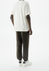 Avslappnad outfit med en ljus krämfärgad t-shirt och mörkgröna joggers med elastiska muddar, kombinerat med vita sneakers och svarta detaljer.