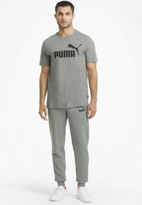 Camiseta de algodón gris con el logo negro de "PUMA" y joggers grises a juego. Ambos artículos presentan un corte relajado y una tela sutilmente texturada.