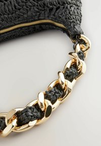 Schwarze geflochtene Handtasche mit einer goldenen Metallkette. Sie verfügt über eine strukturierte Oberfläche und einen Reißverschluss oben.