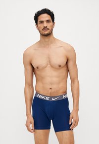 Marineblå Nike herrebokser med en grå elastisk talje, der har Nike-logoet. Materialet ser glat og strækbart ud med et tætsiddende design.