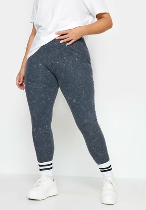 Grijze geribbelde leggings met een gespikkelde textuur, voorzien van een hoge taille en gecombineerd met witte sneakers en zwartgestreepte enkel sokken.
