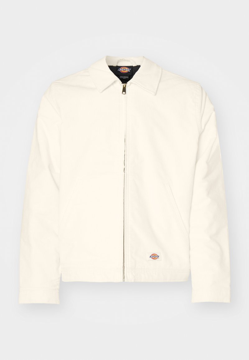 Veste blanche zippée avec un col pointu, texture lisse, poches latérales et un petit patch logo sur la hanche gauche.