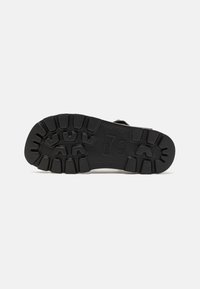 Suola di scarpa in gomma nera con una presa texture e decorata; presenta un logo del marchio. La suola ha una forma arrotondata con profondi modelli di battistrada.