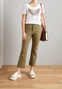 Vit t-shirt med färggrafisk fjäril, olivgröna cropped-byxor och vita plattformssandaler. Brun axelväska med lock.