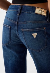 Donkerblauwe spijkerbroek met een hoge taille, voorzien van een label aan de achterkant, twee achterzakken en contrasterende stiksels.