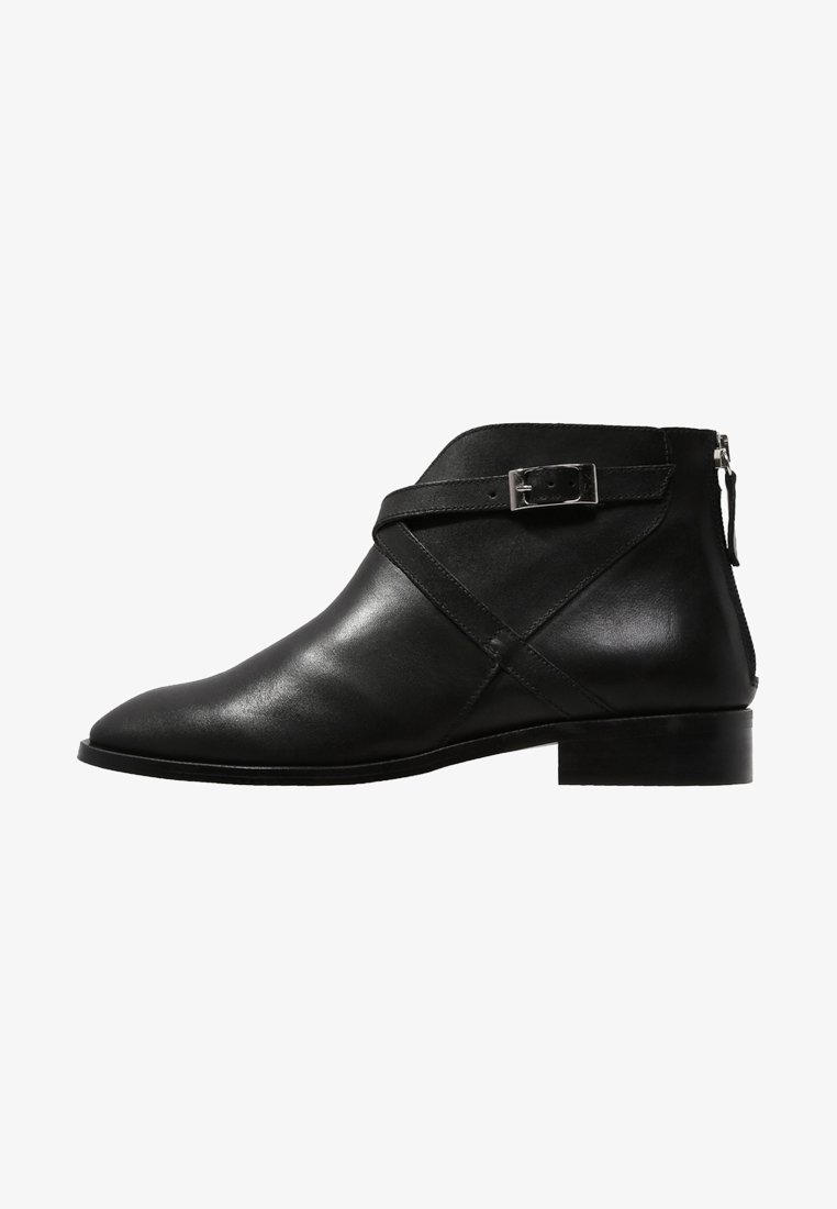 Bottine en cuir noir avec petit talon, bout pointu, bride enveloppante avec boucle argentée et fermeture éclair au dos.