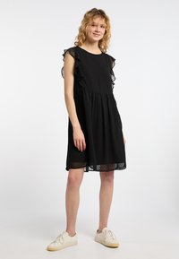 Czarna sukienka z kropkowaną teksturą, marszczonymi, przezroczystymi rękawami i rozkloszowanym dołem, w połączeniu z białymi sneakerami. Prosty, elegancki design.