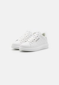 Hvite joggesko med et teksturert design på sidene, flat såle og rund tå. Har snøring og subtil merkevare på siden.