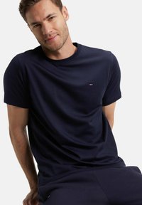 T-shirt bleu marine à manches courtes en tissu lisse, avec un petit logo sur la poitrine. Col rond et coupe décontractée.