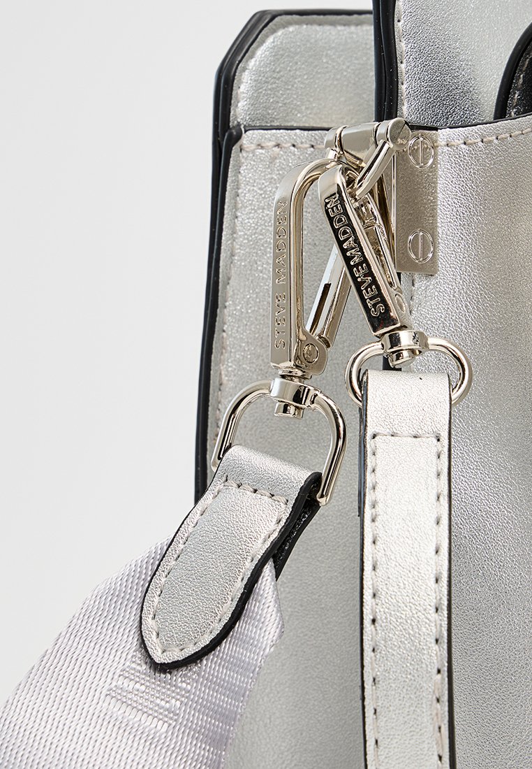 Sac à main argenté métallisé avec des accents noirs, présentant une finition texturée, du matériel argenté et une bandoulière amovible avec une surface lisse.